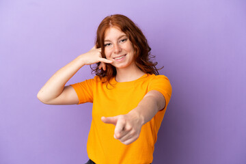 Teenager redhead girl over isolated purple background making phone gesture and pointing front