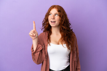 Teenager redhead girl over isolated purple background thinking an idea pointing the finger up