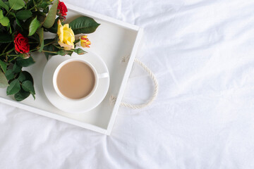 Tray with coffee and a bouquet of flowers on a white bed, copy space.