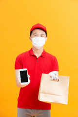 Fototapeta na wymiar Deliveryman in uniform and protective mask holding and showing paper bag and smartphone with empty screen,