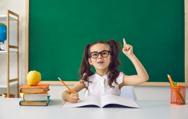 Back to school concept. Little girl schoolgirl with glasses raised her finger up has an idea on the...