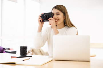 Portrait of beautiful photographer woman working in office holding camera with laptop. Bloger freelance online marketing.