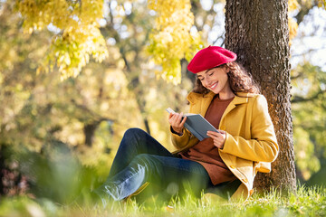 Young woman reading book in park during autumn season