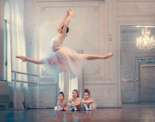 Three little funny ballerinas are looking with delight at gorgeous jump of adult ballerina in ballet class. Image with selective focus and toning - obrazy, fototapety, plakaty