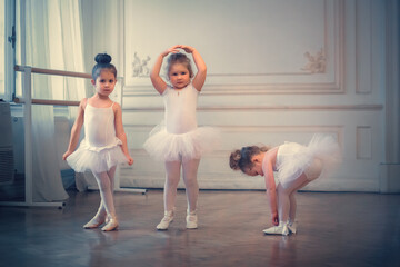 Three funny little ballerinas in tutus are in the ballet class. Image with selective focus and toning © Smolina