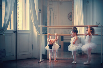 Three funny little ballerinas in tutu are training near the barre. One of them is being naughty....