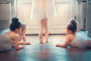 Three little funny ballerinas are looking with delight at feet in pointe shoes of dancing adult ballerina. Image with selective focus and toning