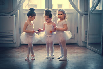 Three funny little ballerinas are eating chocolate candies in the ballet class. Image with...