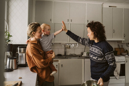 Mamma b&auml;r dotter som g&ouml;r high-five med mamma st&aring;ende i k&ouml;k