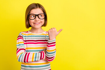 Photo portrait little girl curious showing copyspace with thumb in glasses isolated vibrant yellow color background