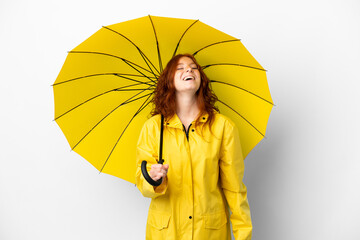Teenager redhead girl rainproof coat and umbrella isolated on white background laughing © luismolinero
