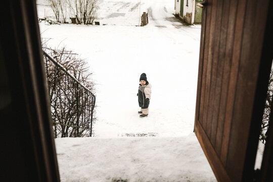 Flicka i overall st&aring;r i sn&ouml;n utanf&ouml;r hus