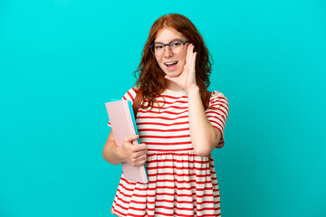 Student teenager redhead girl isolated on blue background with surprise and shocked facial expression