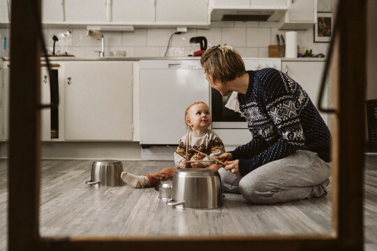 Mamma och dotter leker med kastruller sittande p&aring; golv i k&ouml;k