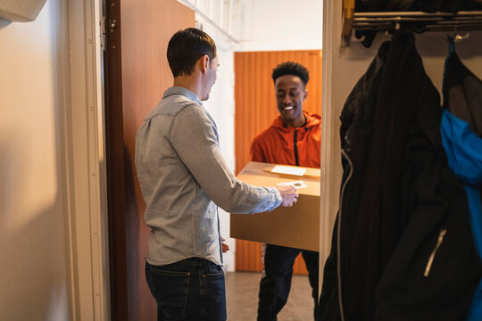 Leende manligt bud levererar paket till man st&aring;ende i trapphus