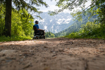 Obraz premium Man on a wheelchair relaxing in nature and looking at mountains on a sunny summer day.