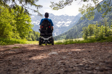 Man on a wheelchair relaxing in nature and looking at mountains on a sunny summer day.