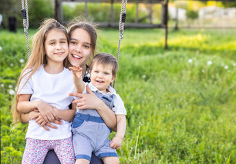 Cheerful children in light clothes ride a street swing in a blooming green home garden and laugh in a happy smile