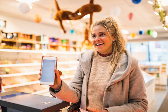 Glad kvinna visar upp smartphone st&aring;ende i aff&auml;r