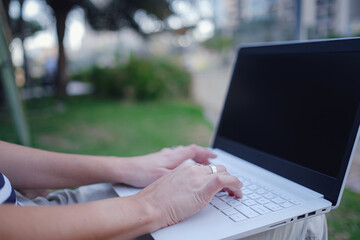 Female hands on laptop, woman types on keyboard sitting in park.