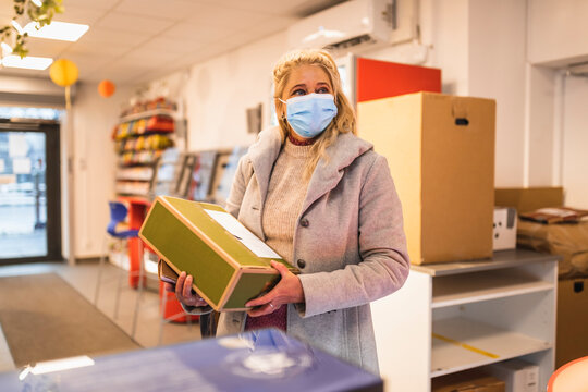 Kvinna med munskydd b&auml;r paket st&aring;ende i butik