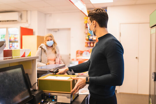 Man med munskydd v&auml;ger paket och pratar med kvinnlig kund i butik