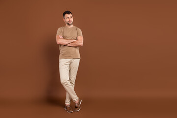 Fototapeta na wymiar Photo of pretty confident young guy dressed beige clothes arms crossed looking empty space isolated brown color background