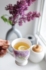 Top view concept of woman hand holding a cup of tea. Lilac flowers on background