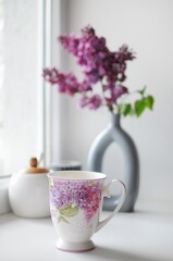 Composition of beautiful cup of tea with lilac flowers on background