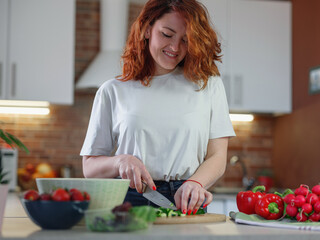 Beautiful redhair young woman is preparing vegetable salad in the kitchen.