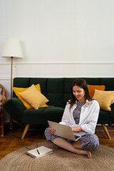 Image of young cheery positive beautiful business woman sitting indoors in office or home office using laptop computer.
