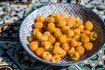 Blue plate full of fresh yellow raspberries on garden table.