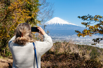 Woman taking a photo of Mount Fuji, with an aerial view of Fuji City. Photo taken from Noroshiba,...