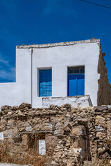 Small white house with blue color door and window, wooden frames on whitewashed  wall, greek island architecture, clear blue sky background. Greece.