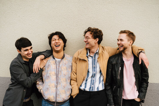 Glada v&auml;nner h&aring;ller armarna om varandra st&aring;ende vid v&auml;gg