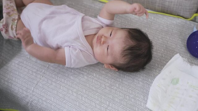close up shot innocent baby girl is lying on the home sofa as its parent is removing her pants and undoing the bodysuit button to change diapers.