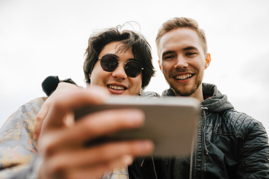 Glada manliga v&auml;nner tar selfie med smartphone