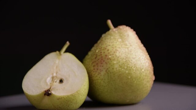 A whole pear and half a pear are lying next to each other. Ripe juicy yellow fruits with drops of water