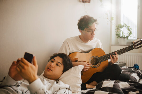 Ung man anv&auml;nder smartphone medan kompis spelar gitarr bredvid