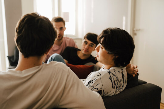 Ung man pratar med v&auml;nner sittande i vardagsrum hemma