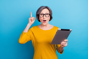 Portrait of attractive trendy cheerful amazed woman using tablet pointing up isolated over bright...