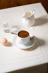 Coffee, boiled egg, milk and glass of water on linen tablecloth, breakfast