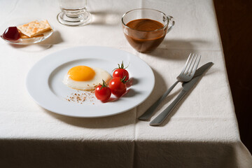 Fried egg with tomatoes on white plate, breakfast dining table