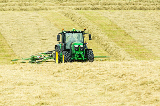 John Deere Tractor Working In A Field With A Twin Rotor Hay Turner Or Tedder Attachment During A Hay Harvest