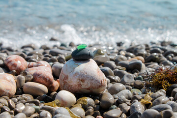 The pyramid is built on a pebble beach of sea pebbles with a matte smooth green glass at the top. Against the background of waves, water splashes and foam © Yulia
