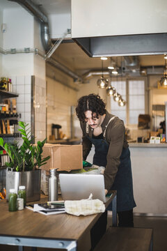 Manlig &auml;gare med f&ouml;rkl&auml;de arbetar p&aring; laptop st&aring;ende i butik