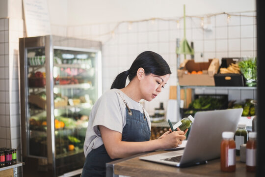 Kvinnlig entrepren&ouml;r med f&ouml;rkl&auml;de sitter vid dator i butik