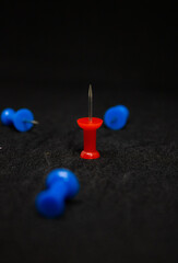 Blue pushpins against a red pushpin in a black background