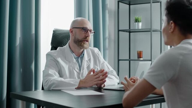 Bearded doctor explains problem to patient sitting on chair