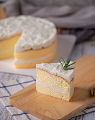 Coconut cake - slice of homemade coconut cake topping with rosemary on wooden board.
